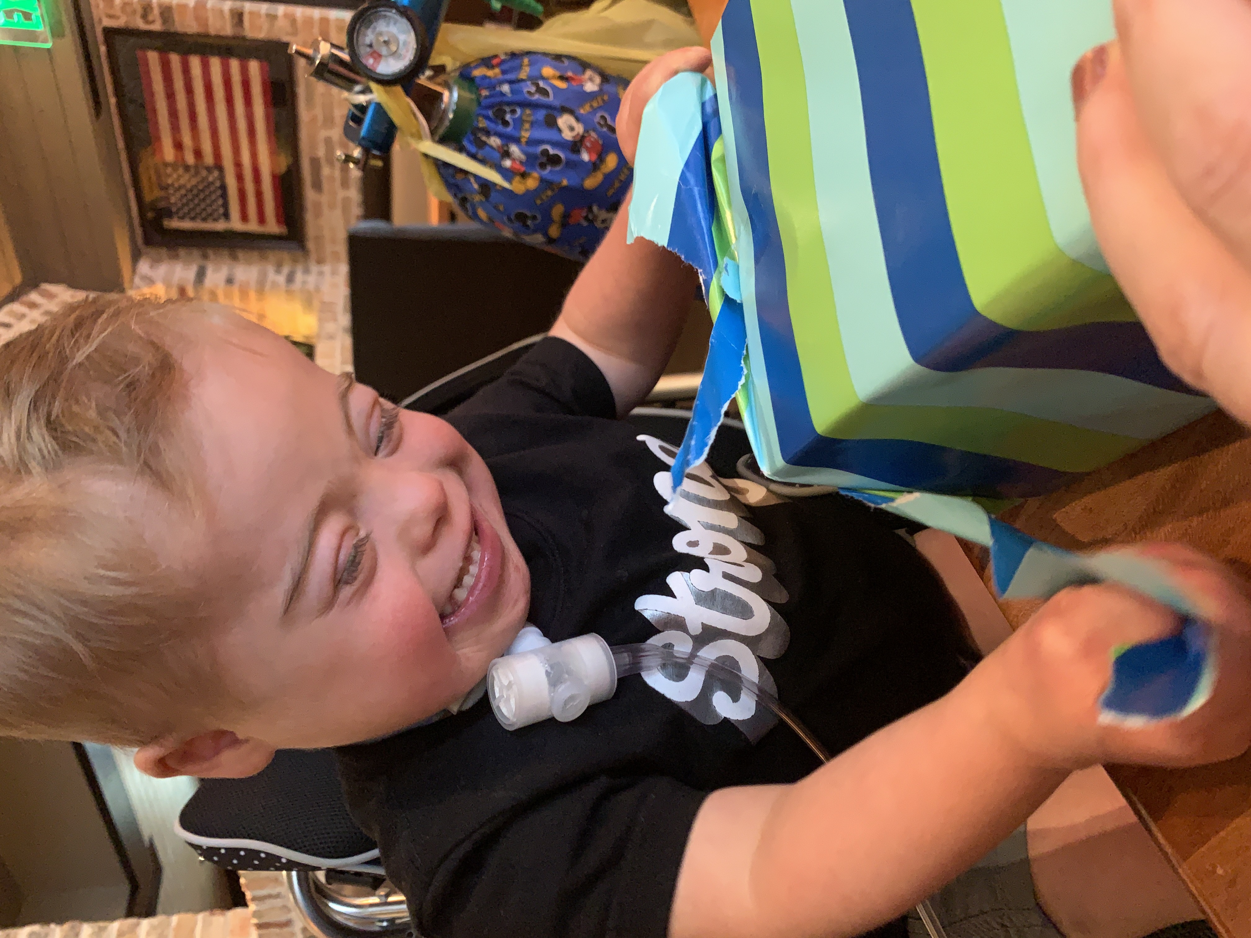 Boy with Down syndrome and trach smiling while opening gift